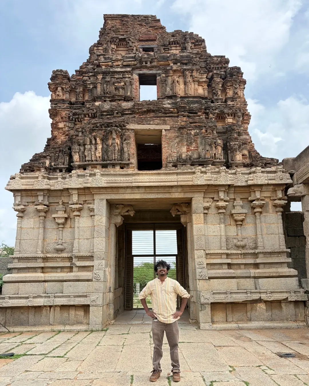 जुन्या दगडी मंदिराच्या गोपुरासमोर कमरेवर हात ठेवून उभे संपादक